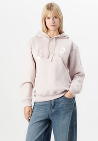Roza hoodie s "GAP" logotipom u reflektirajućim slovima, s kangaroo džepom i kapuljačom s užetom, uparen s svijetlosivim, širokim trapericama.
