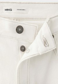 Gros plan sur la ceinture d'un jean en denim blanc avec des boutons métalliques étiquetés "MNG Jeans Established 1984" et une étiquette de taille visible EU 36 USA 4 MEX 3.