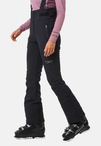 Zwarte skibroek met bretels, tapered fit, met ritssluiting zak en logo detail op de dij. G gedragen met zwarte skibotten.