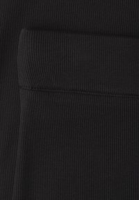Close-up of black ribbed fabric with visible stitching and a folded cuff or edge detail.