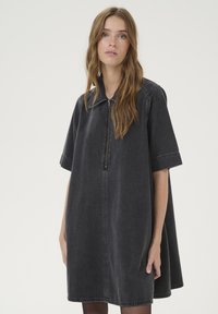 Svart denimklänning med dragkedja i halsen, korta ärmar och en utflödesdesign. Mjuk struktur och subtila sömnadsdetaljer förhöjer utseendet.