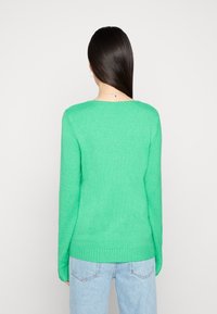 Green knit sweater with a round neckline and long sleeves. Soft texture, ribbed cuffs and hem, paired with light blue jeans.