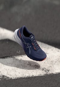 Baskets de course de marine avec une tige en maille, accents gris et détails rouges. Présente une semelle rembourrée et un design respirant, surélevé pour faciliter le mouvement.