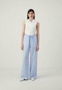 Λευκό αμάνικο πουκαμισάκι με cropped σχέδιο, σε συνδυασμό με ψηλόμεσα ανοιχτόχρωμα μπλε παντελόνια με φαρδύ μπατζάκι και λευκά sneakers.