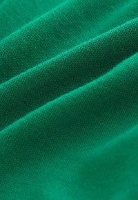 Tissu tricoté vert avec une texture de maille fine visible et des plis doux créant des lignes diagonales.