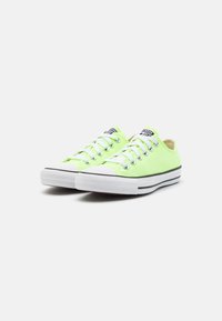 Sneaker in tela verde neon con suola in gomma bianca, lacci bianchi e accenti di striscia nera, angolati a sinistra su sfondo bianco uniforme.