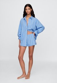 Camisa oversize a rayas azules con detalle recortado, combinada con pantalones cortos a juego. Hecha de tela ligera, que muestra un ajuste relajado y un estilo casual.