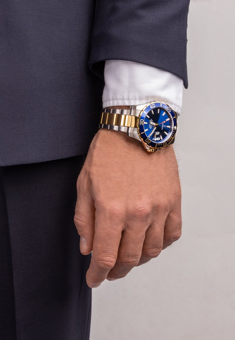 Montre en acier inoxydable et en or avec un cadran bleu, dotée d'un bracelet en argent et en or, de marqueurs lumineux et d'un affichage de la date à 3 heures.