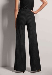 Zwarte broek met pinstripes en wijd uitlopende pijpen, gekenmerkt door een hoge taille, zijzakken en een soepele textuur, gecombineerd met spitse zwarte hakken.