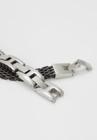 Bracciale in metallo con anelli opachi argentati intrecciati e design a catena, dotato di un meccanismo di chiusura per una chiusura sicura.