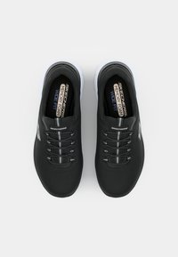 Scarpe da ginnastica nere con una tomaia testurizzata, lacci elastici e suola bianca. Presentano le etichette "Memory Foam" e "Wide Fit" all'interno.