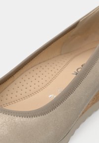 Beżowy baletki z gładką, syntetyczną cholewką, miękką perforowaną wkładką oraz subtelnym teksturowanym detalem wzdłuż krawędzi.