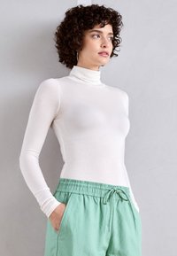 Long-sleeve white turtleneck top made of soft fabric, paired with loose mint green pants featuring an elastic waistband and pockets.