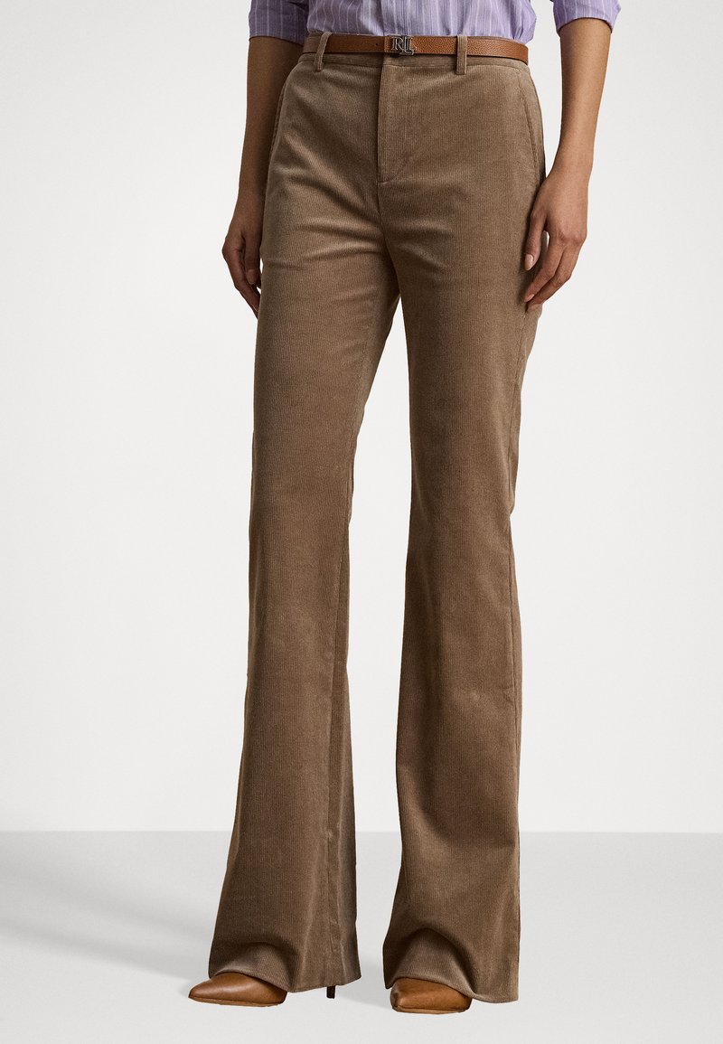 Pantaloni a zampa d'elefante in corduroy marrone con righe verticali, dotati di zip frontale e passanti per cintura. Indossati con una camicia a maniche lunghe di colore viola chiaro.