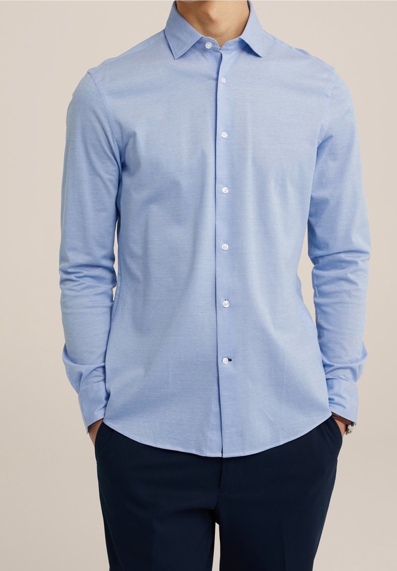 Camisa de manga larga azul claro con cuello puntiagudo, frente abotonado y dobladillo redondeado. Hecha de una tela suave y ligeramente texturizada.