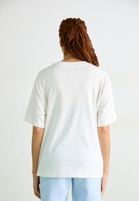 T-shirt en coton blanc surdimensionné avec des manches courtes et un col rond, texture lisse et design simple. La vue de dos ne montre aucun motif ni graphique.