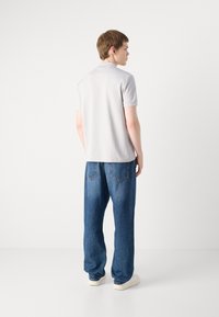 Polo shirt gris clair à manches courtes associé à un jean en denim bleu ample. La tenue présente un design décontracté avec des détails de couture subtils.