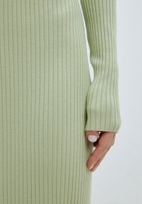 Robe en maille côtelée vert clair à manches longues. Présente une coupe ajustée et des poignets allongés, mettant en valeur une texture douce et des lignes verticales.