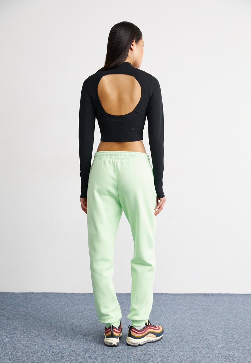 Schwarzes langärmliges Crop-Top mit einem kreisförmigen Ausschnitt am Rücken, kombiniert mit mintgrünen Jogginghosen und mehrfarbigen Sneakers.
