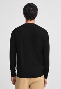 Maglione nero in maglia con maniche lunghe e scollatura rotonda. Presenta polsini e orlo a coste per una vestibilità aderente. Texture liscia, design semplice.