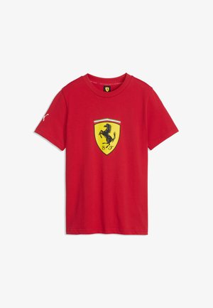 Czerwona koszulka z krótkim rękawem z żółtym logo Ferrari i czarnym koziołkującym koniem z przodu oraz małym białym logo Puma na lewym rękawie.