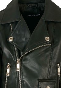 Giacca da moto in pelle nera con accessori in argento, cerniera asimmetrica, colletto a revers e tasca a patta. La texture appare liscia e leggermente lucida.