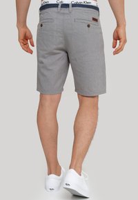 Grå og hvide stribede shorts har en flad front, to baglommer med knapper, og er stylet med hvide sneakers.
