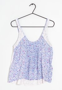 Top senza maniche floreale in tessuto bianco e blu, caratterizzato da un design arricciato con piccoli fiori rosa e dettagli in pizzo sui lati.