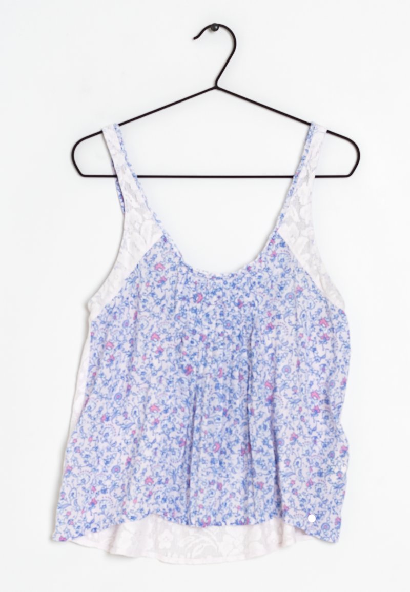 Top senza maniche floreale in tessuto bianco e blu, caratterizzato da un design arricciato con piccoli fiori rosa e dettagli in pizzo sui lati.
