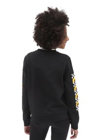 Sudadera negra con escote redondo, que presenta patrones de cuadros y girasoles en las mangas y una tela suave y texturizada.