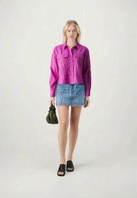 Fuksia linas marškiniai su sagų uždarymu ir krūtinės kišenėmis, derinami su džinsiniu mini sijonu su suplėšytu kraštu, juodais šlepetėmis ir žalia kuprine.