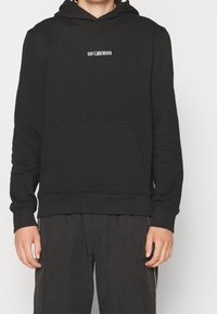 Felpa nera in misto cotone, con tasca frontale, cappuccio con coulisse e logo testuale bianco sul petto. Polsini e orlo a costine.