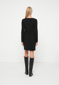 Čierne šaty s dlhým rukávom, štvorcovým dekoltom a priliehavým strihom. Hladká tkanina; dĺžka po kolená bez viditeľných vzorov.