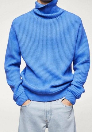 Maglione blu lavorato a maglia con collo alto e texture a coste, dotato di maniche lunghe e vestibilità ampia, abbinato a jeans in denim chiaro.