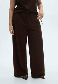 Brown wide-leg trousers in soft fabric, featuring an elastic waistband with drawstrings. Paired with pointed-toe shoes.
