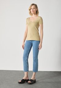 Beige kortermet V-hals t-skjorte, lyseblå rette jeans og svarte glidesandaler med treaksyner og metallnagle.