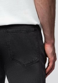 Mustat farkut näyttävät takaa, jossa näkyy takatasku ja vyötärönauha. Kangas on sileäpintaista ja hyvin istuvaa.