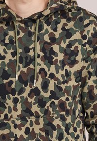 Felpa con cappuccio verde oliva con motivo mimetico con accenti neri e marroni, trama a coste, tasca a marsupio e coulisse a contrasto.