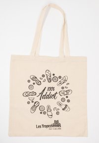 Borsa a tracolla in tela di un beige chiaro con grafiche in inchiostro nero di calzature e la scritta "100% Addict" centrata con il nome del brand in basso.