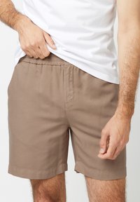 Bruine katoenen shorts met een elastische tailleband, zijzakken en een rechte snit. De stof lijkt glad met minimale details.