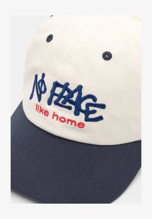 Fehér és sötétkék baseballsapka, hímzett "Nincs olyan hely, mint otthon" felirattal kék és piros színben. Ívelt karimával és varrott részletekkel rendelkezik.