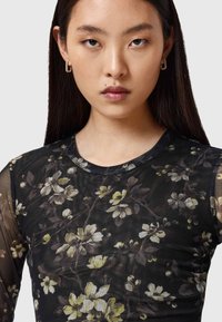 Μαύρο τοπ από δίχτυ με λουλουδάτο μοτίβο σε κίτρινο και λευκό, με στρογγυλή λαιμόκοψη και εφαρμοστά μακριά μανίκια. Περιλαμβάνει διαφανή υφή ως διακοσμητικό στοιχείο.