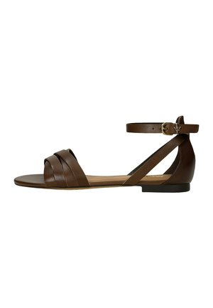 Brązowa płaska sandał z przednimi paskami, paskiem na kostkę i złotą klamrą na białym tle.