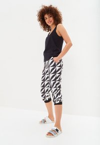 Sort ærmeløs top parret med hvid- og sortmønstrede joggers med geometriske former. Hvide slide sandaler med blå accenter.
