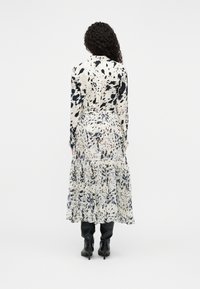 Φλοράλ φόρεμα σε λευκό με μπλε και μαύρα σπρέι μοτίβα, μακρυά μανίκια, στρωματοποιημένη φούστα και εφαρμοστή μέση, συνδυασμένο με μαύρες μπότες μέχρι το γόνατο.