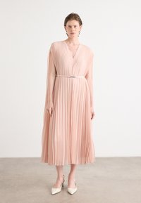 Pleated midi dress in soft pink with a deep v-neck, cap sleeves, and a matching belt. Paired with cream pointed-toe heels.