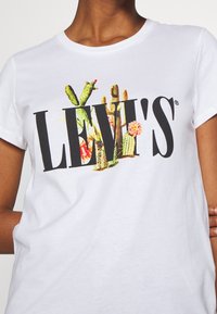 Biały bawełniany t-shirt z czarnym logo „LEVI'S” oraz kolorowymi grafikami kaktusów i kwiatów wkomponowanymi w projekt. Krótkie rękawy.