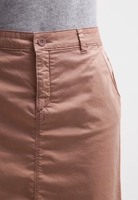 Gonna marrone chiaro in tessuto leggero e liscio con chiusura a bottoni, tasche laterali e cuciture ordinate lungo le cuciture, caratterizzata da una vestibilità aderente.