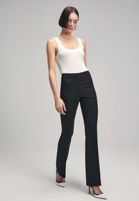 Zwarte slim fit broek met een gladde textuur, met een recht ontwerp. Gepaard met een witte geribde tanktop. Hakken met een spitse neus.