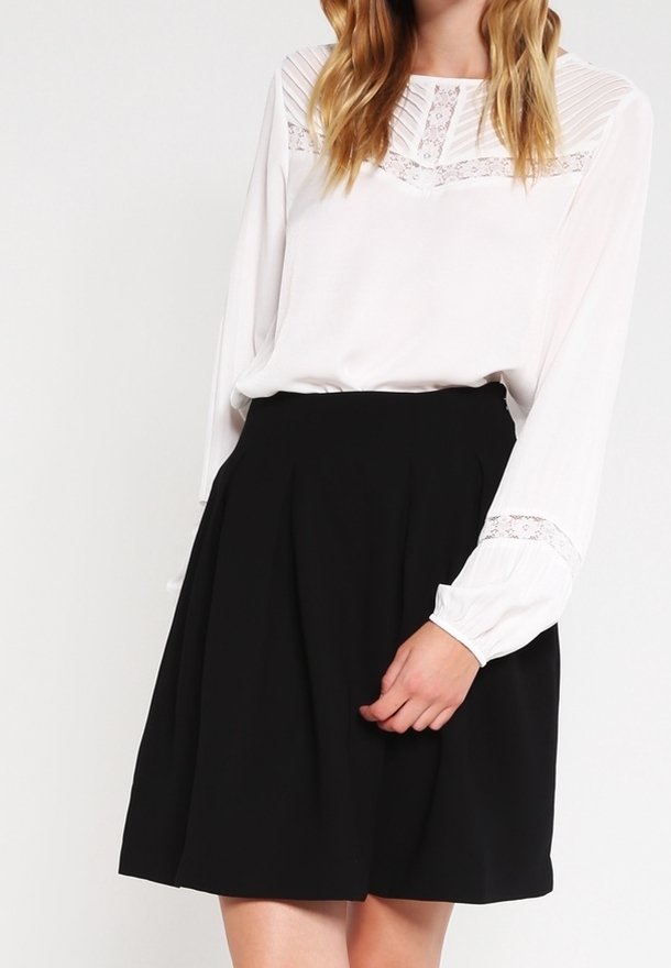 Blusa bianca con dettagli testurizzati e maniche lunghe, abbinata a una gonna nera fino al ginocchio con pieghe.